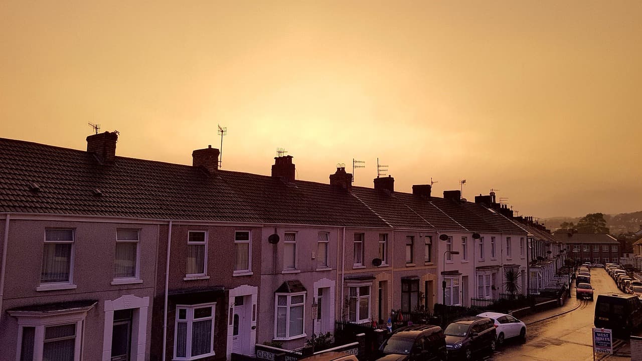 Row of terraced houses on a sloping residential street at sunset, with cars parked along the kerb