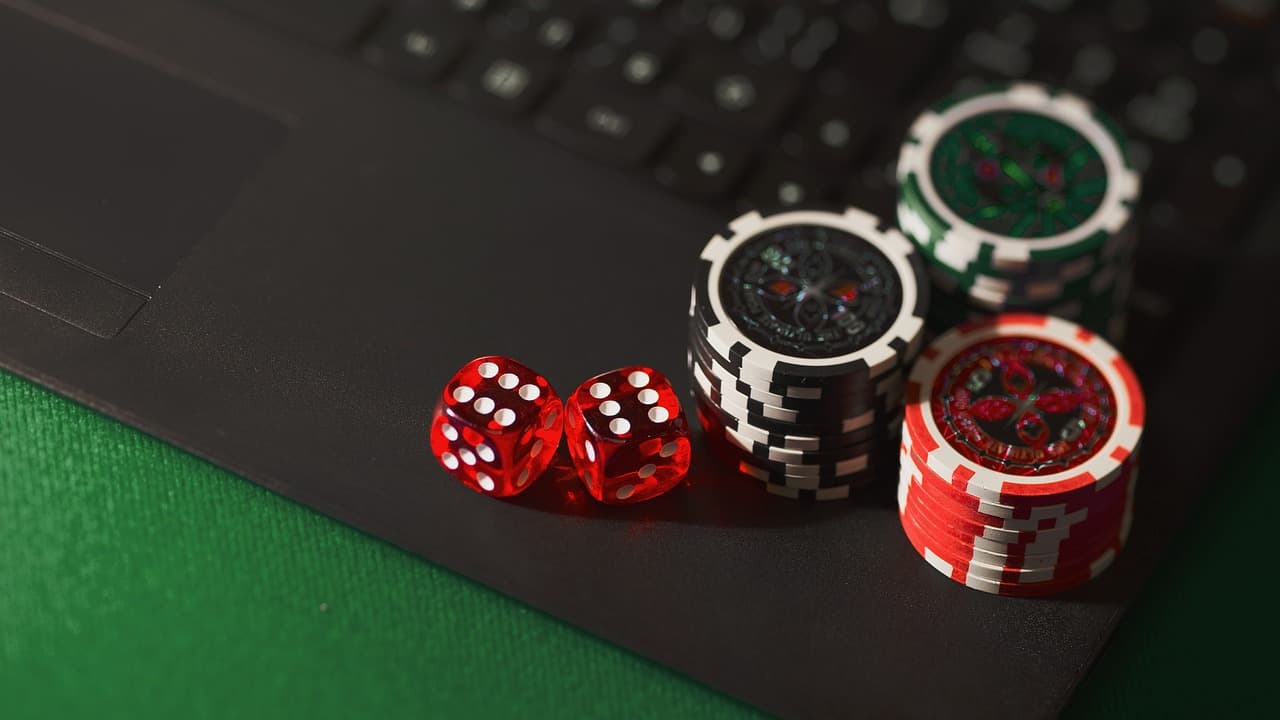 Two red dice and stacked casino chips resting on a black laptop keyboard against a green background