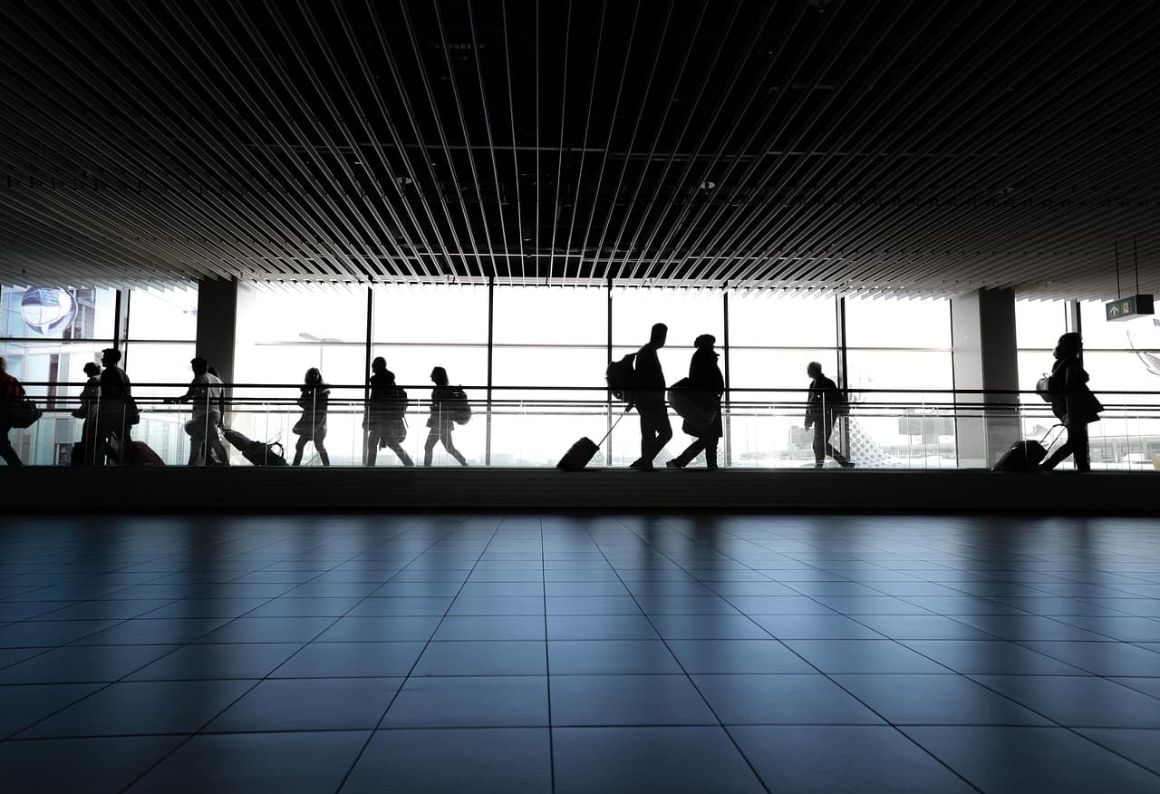 Silhouetted passengers with luggage walking along a glass-walled airport terminal walkway