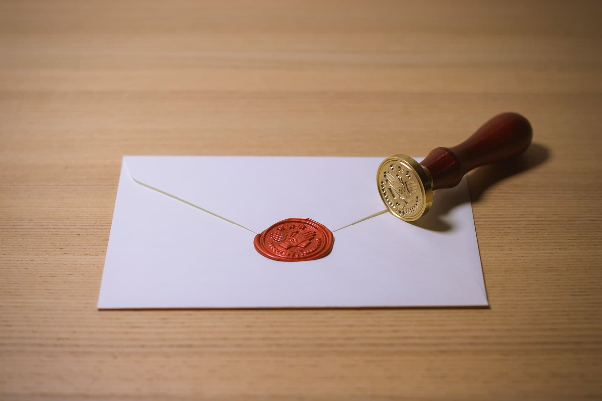 White envelope closed with a red wax seal, next to a brass and wood seal stamp on a desk