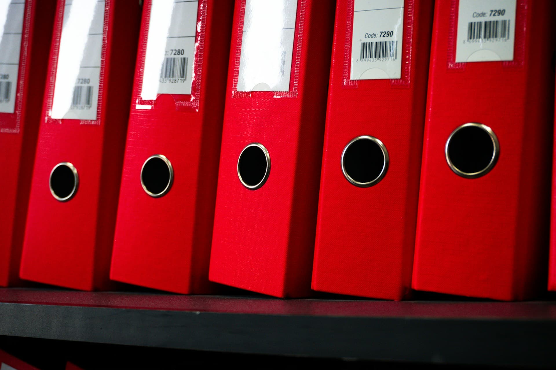 Row of red lever arch files lined up on a shelf with blank spine labels